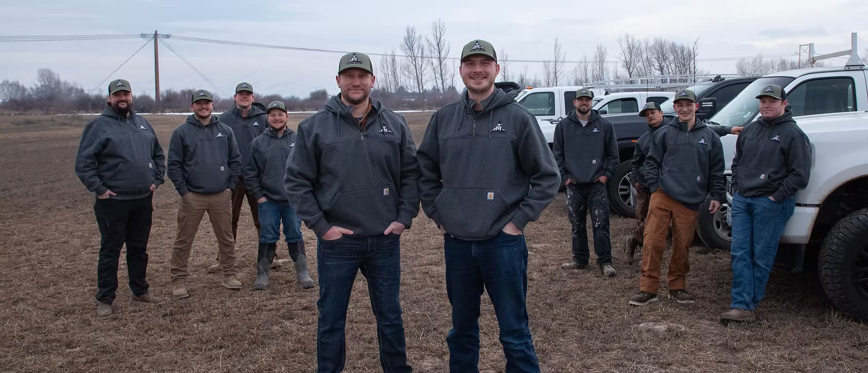 The full TM Construction crew lined up with arms crossed in front of their fleet of trucks