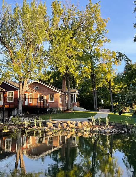 The Brickhouse Nursery reflected in its pond, framed by mature trees in early autumn