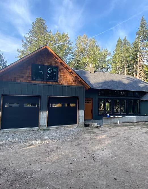 Modern mountain home with dark board-and-batten siding, cedar shingles and a two-car garage, set among pines
